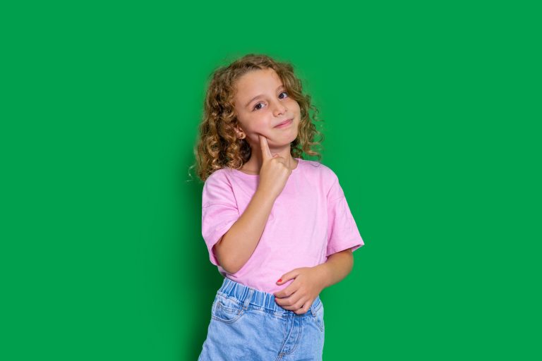 Niña con expresión pensativa y traviesa sobre fondo verde, ilustrando el comportamiento de qué hacer cuando mi hijo me miente.