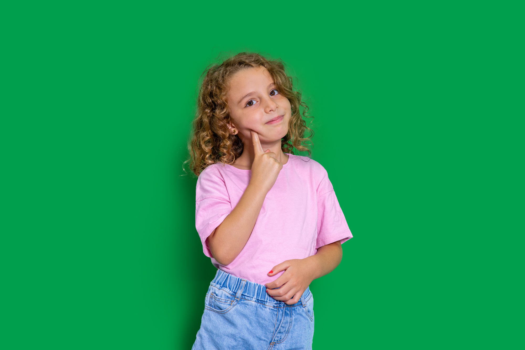 Niña con expresión pensativa y traviesa sobre fondo verde, ilustrando el comportamiento de qué hacer cuando mi hijo me miente.
