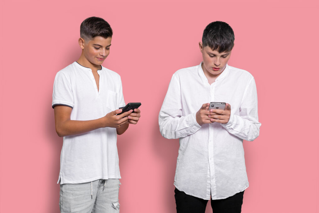 Dos jóvenes con adicción a las pantallas, distraídos por sus dispositivos móviles y desconectados de su entorno.
